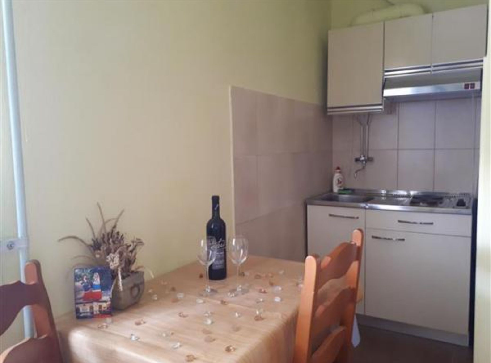 A dining area with a table set for two, a bottle of wine, and a vase with dried flowers.
