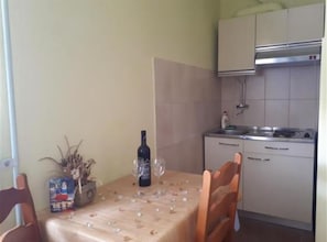 A dining area with a table set for two, a bottle of wine, and a vase with dried flowers. - Apartmani Borić (Orebic)