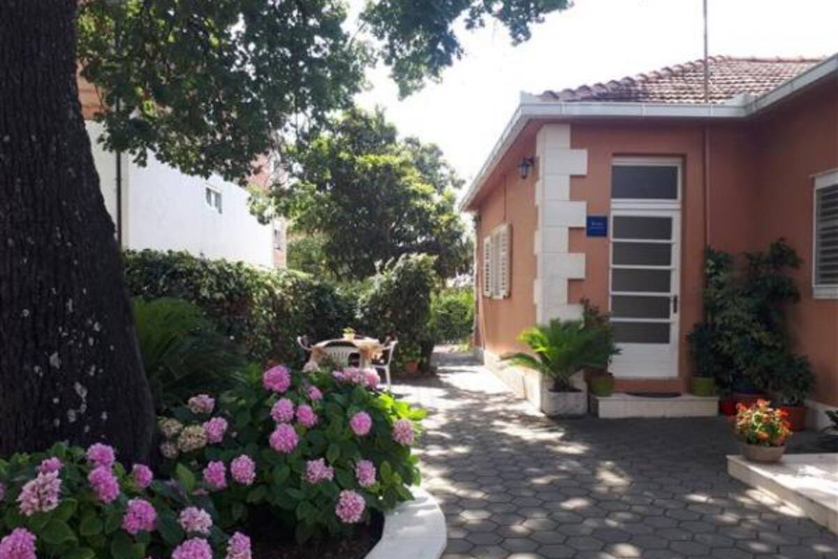 A building with a tiled roof, a door with a window, and a small garden with pink flowers.