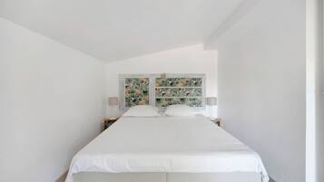 Quarto minimalista com uma cama de casal, roupa de cama branca e cabeceira decorativa com padrão de folha tropical.