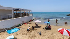 A beach with a building labeled 'Kiosko El Tierno,' people on the sand, and umbrellas. - Bohemian Nights by Fidalsa (Torrevieja)