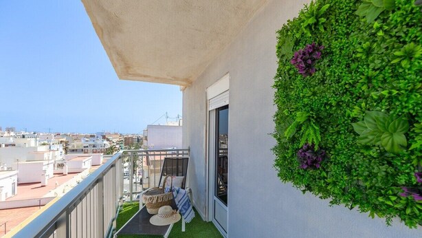 A balcony with a green wall, a small table with a basket, and a view of the cityscape. - Bohemian Nights by Fidalsa (Torrevieja)