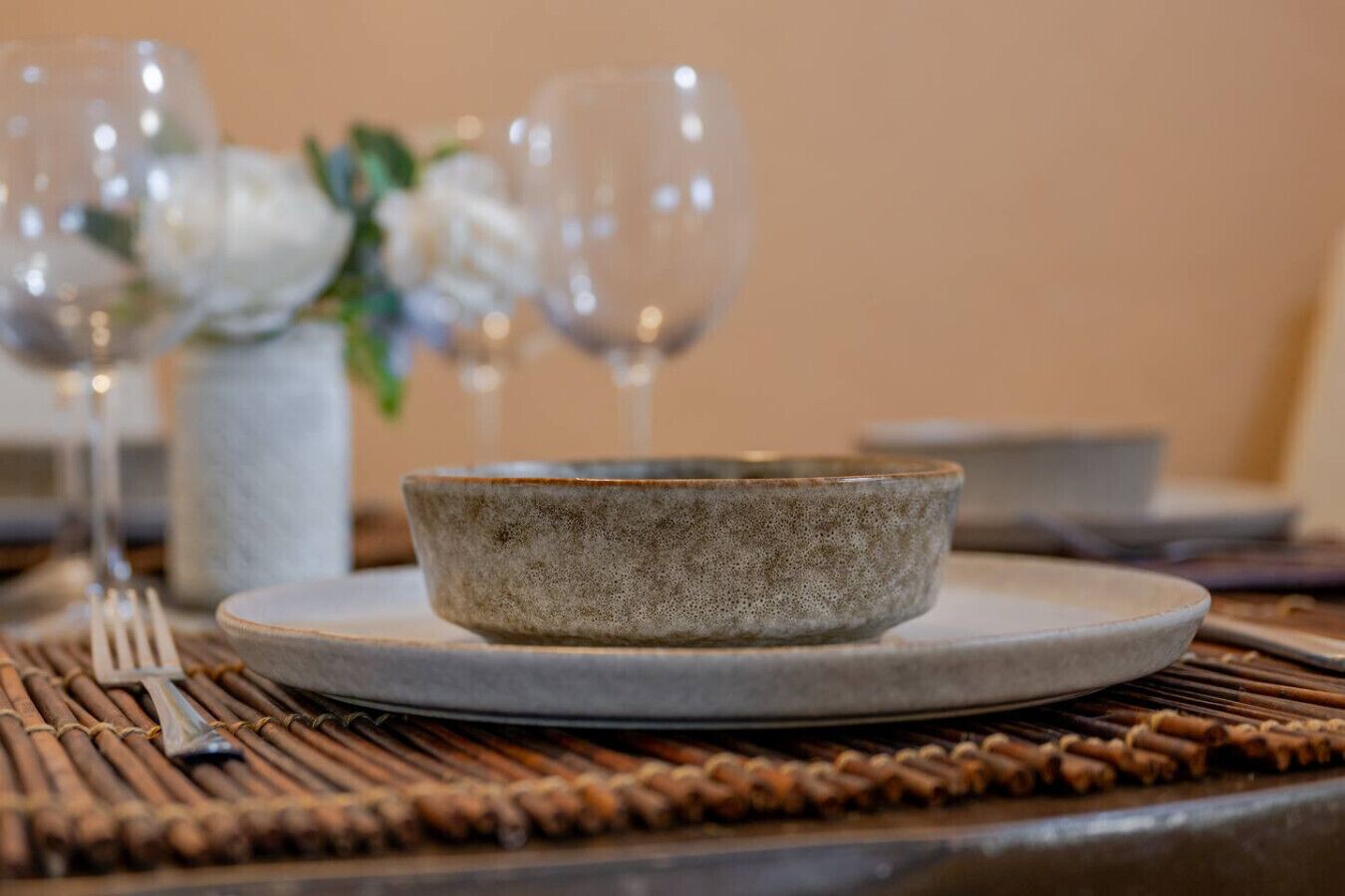 Un tavolo da pranzo con una ciotola di ceramica, una forchetta e bicchieri da vino.