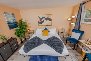 A bedroom with a large bed, bedside tables, a chair, a desk, and a plant. - Chic Urban Escape : Workspace • Park • Downtown (Sarasota)