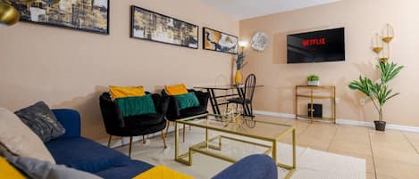 A living room with a sofa, armchairs, a coffee table, a TV, and artwork on the wall.
