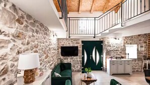 Ein geräumiger Wohnbereich mit Steinwand, einem grünen Sofa, einem Couchtisch und einer Küchenzeile mit weißen Schränken.