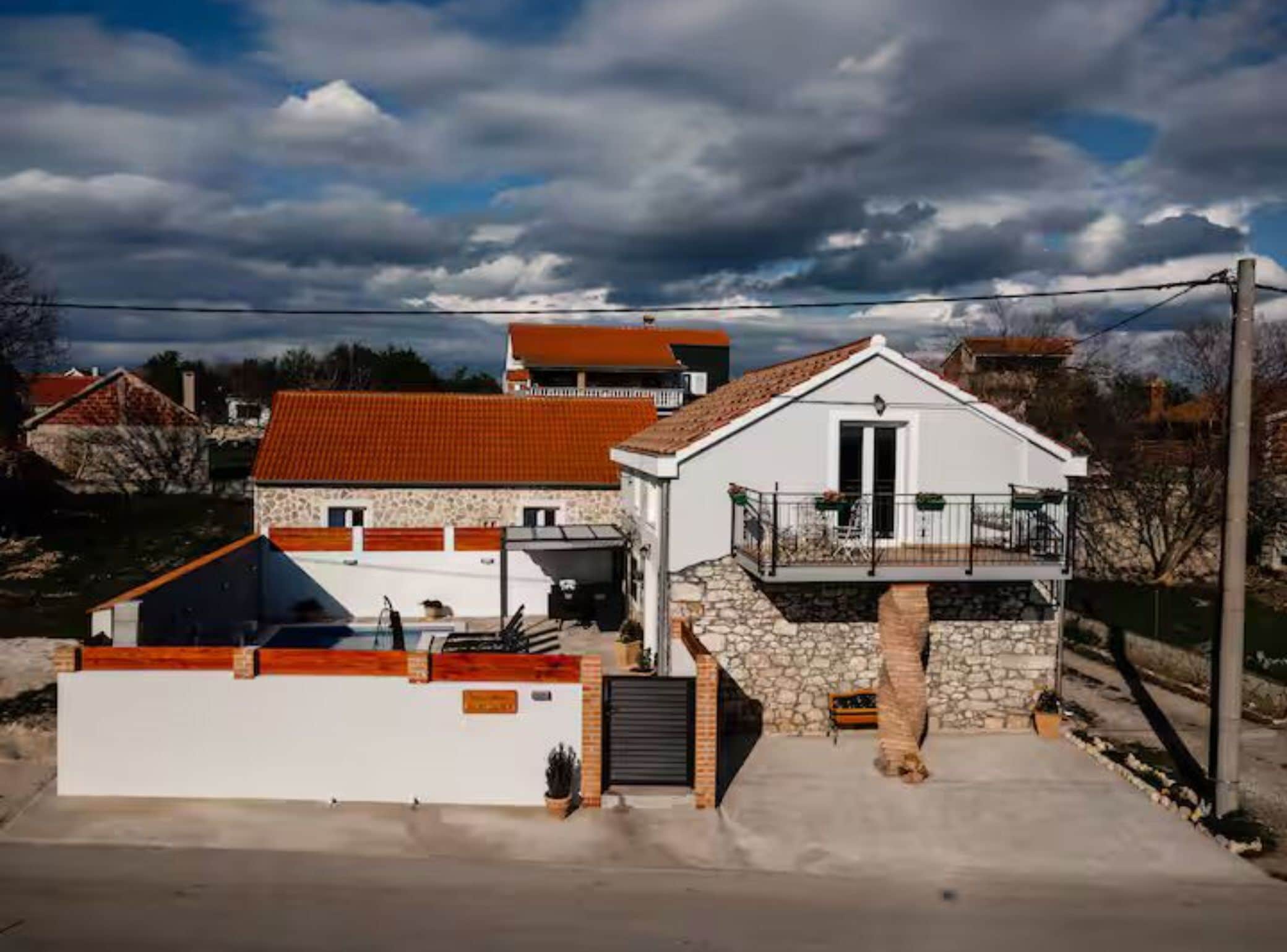 Une maison à deux étages avec une façade en pierre, un toit recouvert de tuiles rouges et un balcon.