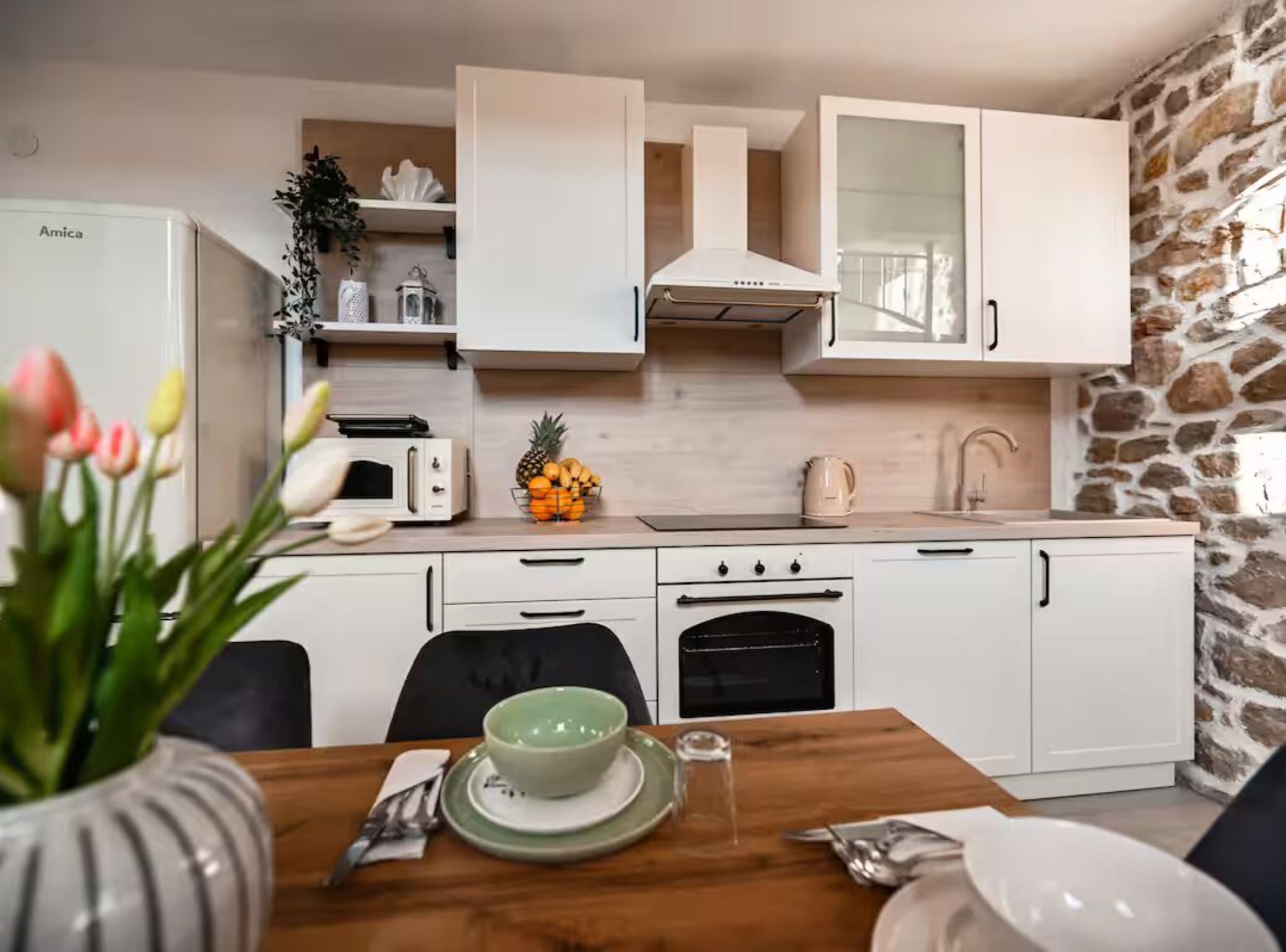 Een moderne keuken met witte kasten, een inbouwoven, een magnetron en een stenen muur.