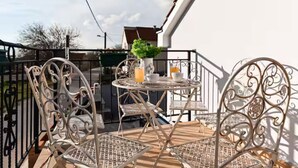 Ein Balkon im Freien mit Metallstühlen und einem Tisch, einer Topfpflanze und einem Getränk auf dem Tisch.