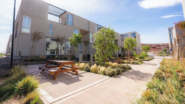 Een modern gebouw met een plat dak, meerdere ramen en een verharde looppad met bankjes.