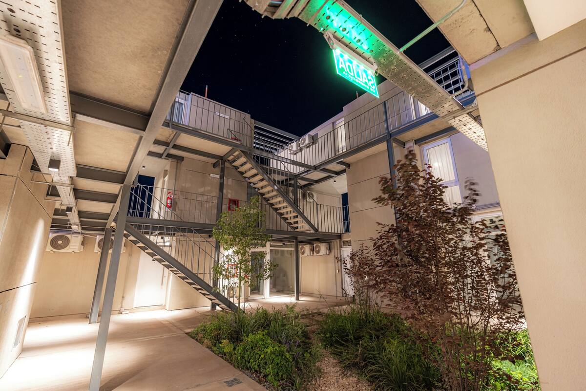 Un edificio de varios niveles con escaleras exteriores, un letrero de neón y algo de vegetación.