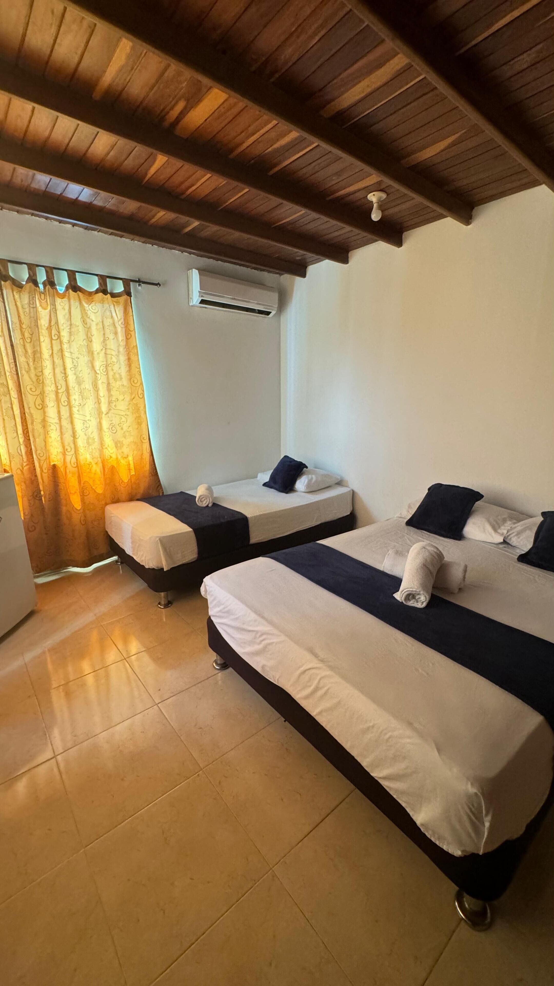 A room with two beds, a ceiling fan, an air conditioning unit, and a curtain.