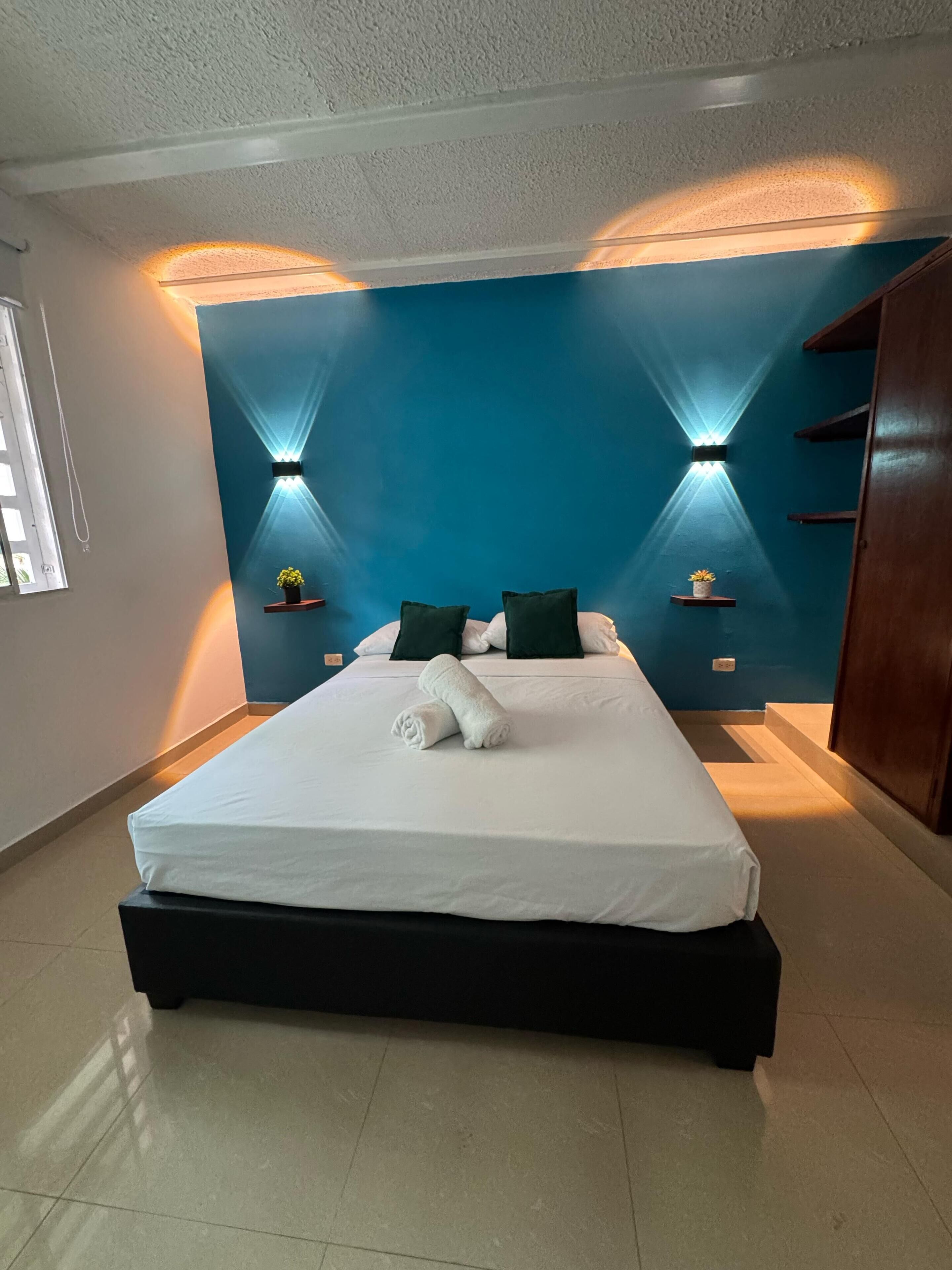 A modern bedroom with a large bed, two wall-mounted lights, and a blue accent wall.