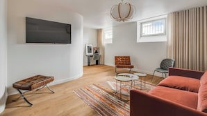 Ein modernes Wohnzimmer mit Flachbildfernseher, gepolstertem Sitzbank, gemustertem Teppich und einem roten Sofa.