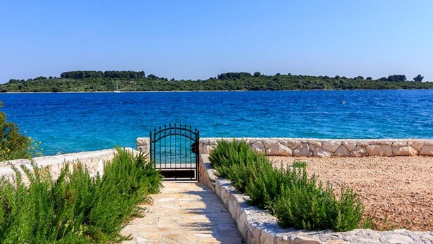 A stone pathway leading to a gate by a clear blue sea with a distant green island. - Villa Renata (Okrug)