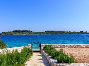 A stone pathway leading to a gate by a clear blue sea with a distant green island.