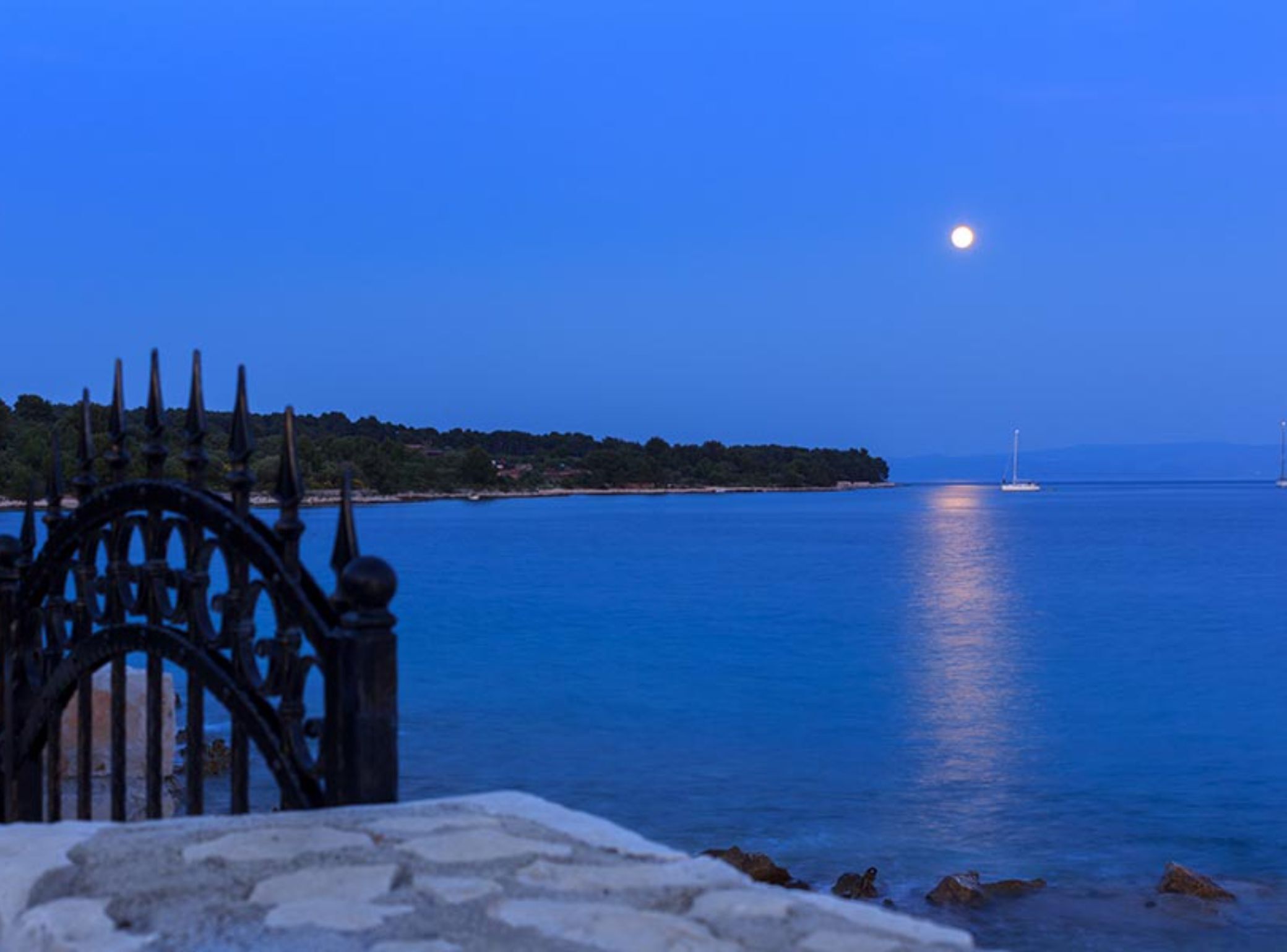 A coastal scene with a clear view of the sea, a distant island, and a moon in the sky.