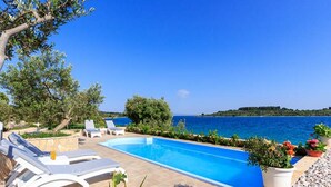 A pool with lounge chairs, a view of the sea, and a stone pathway. - Villa Renata (Okrug)