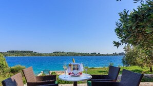 A table with wicker chairs, a bottle, and glasses, overlooking a body of water. - Villa Renata (Okrug)