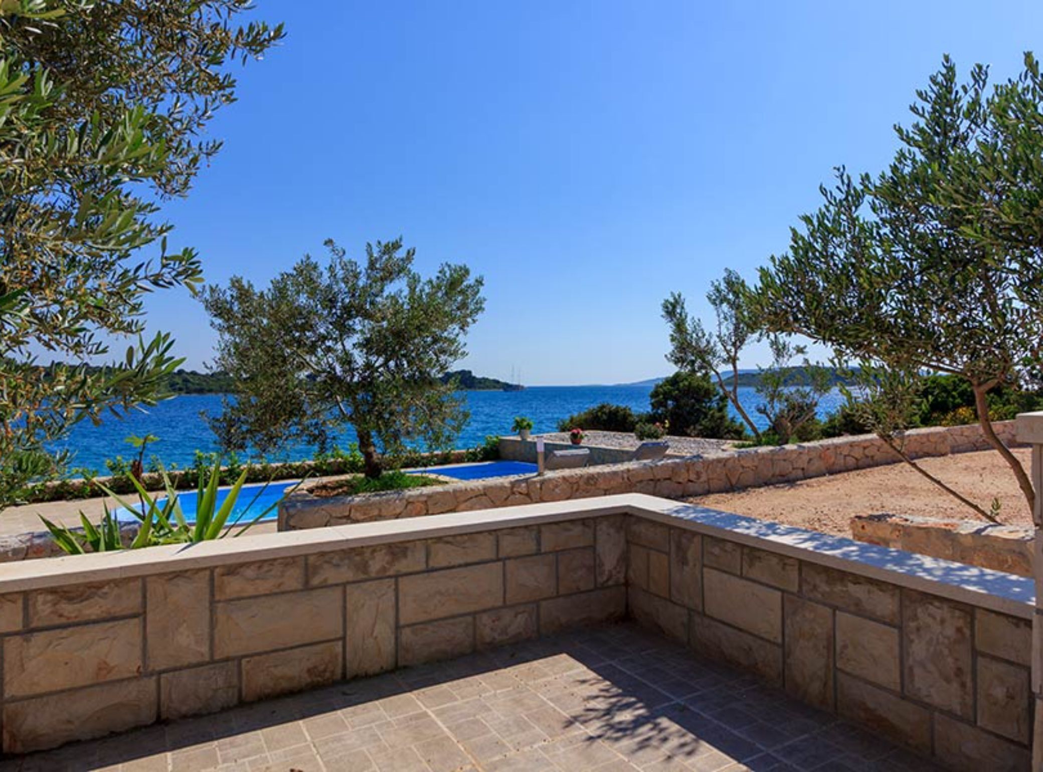 A stone pool with a view of the sea, surrounded by trees and a stone wall.