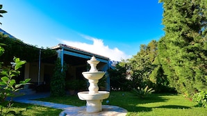 Uma fonte de pedra num jardim, com um edifício ao fundo.