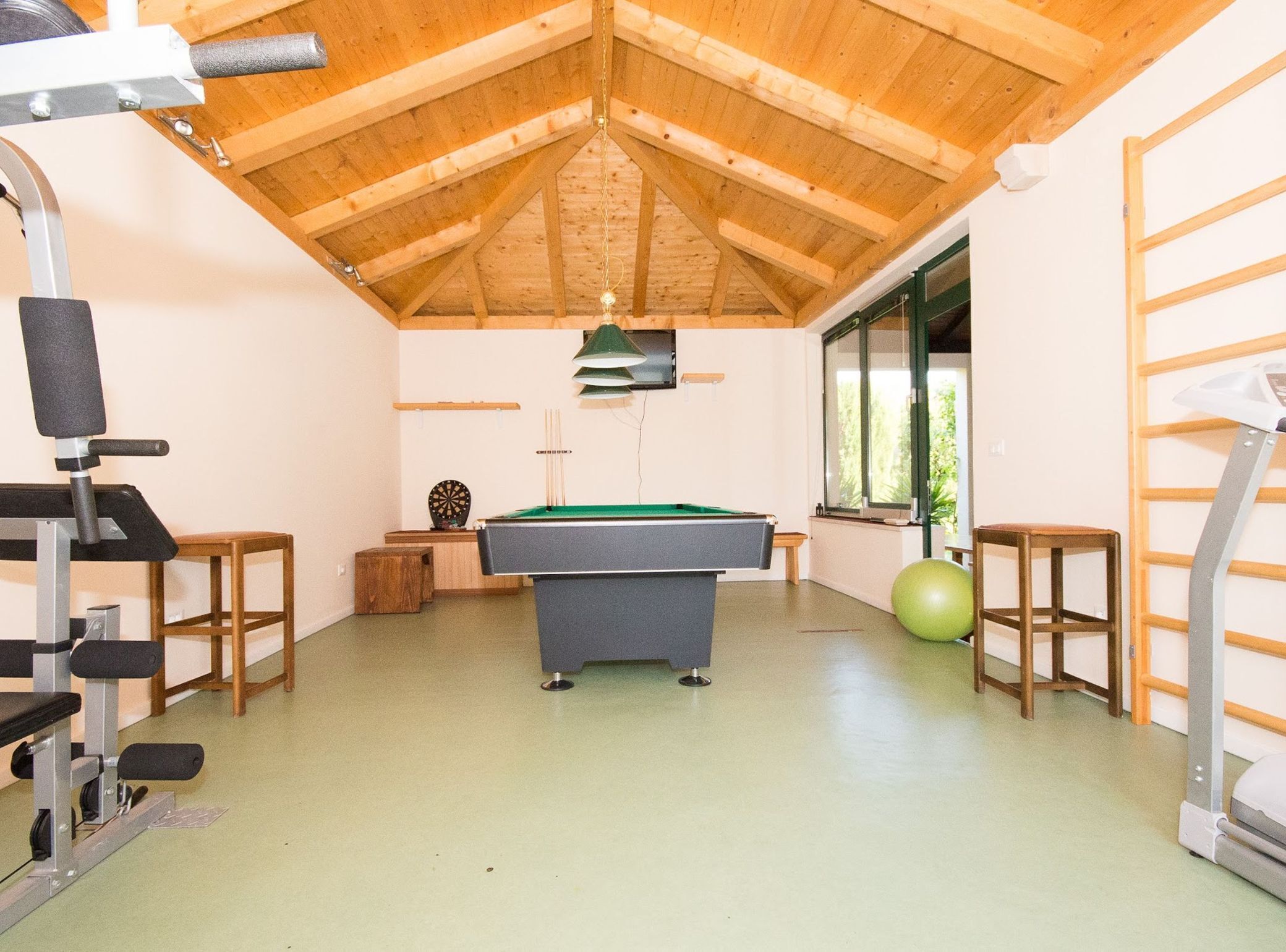 A room with a pool table, exercise equipment, and a window with a view.