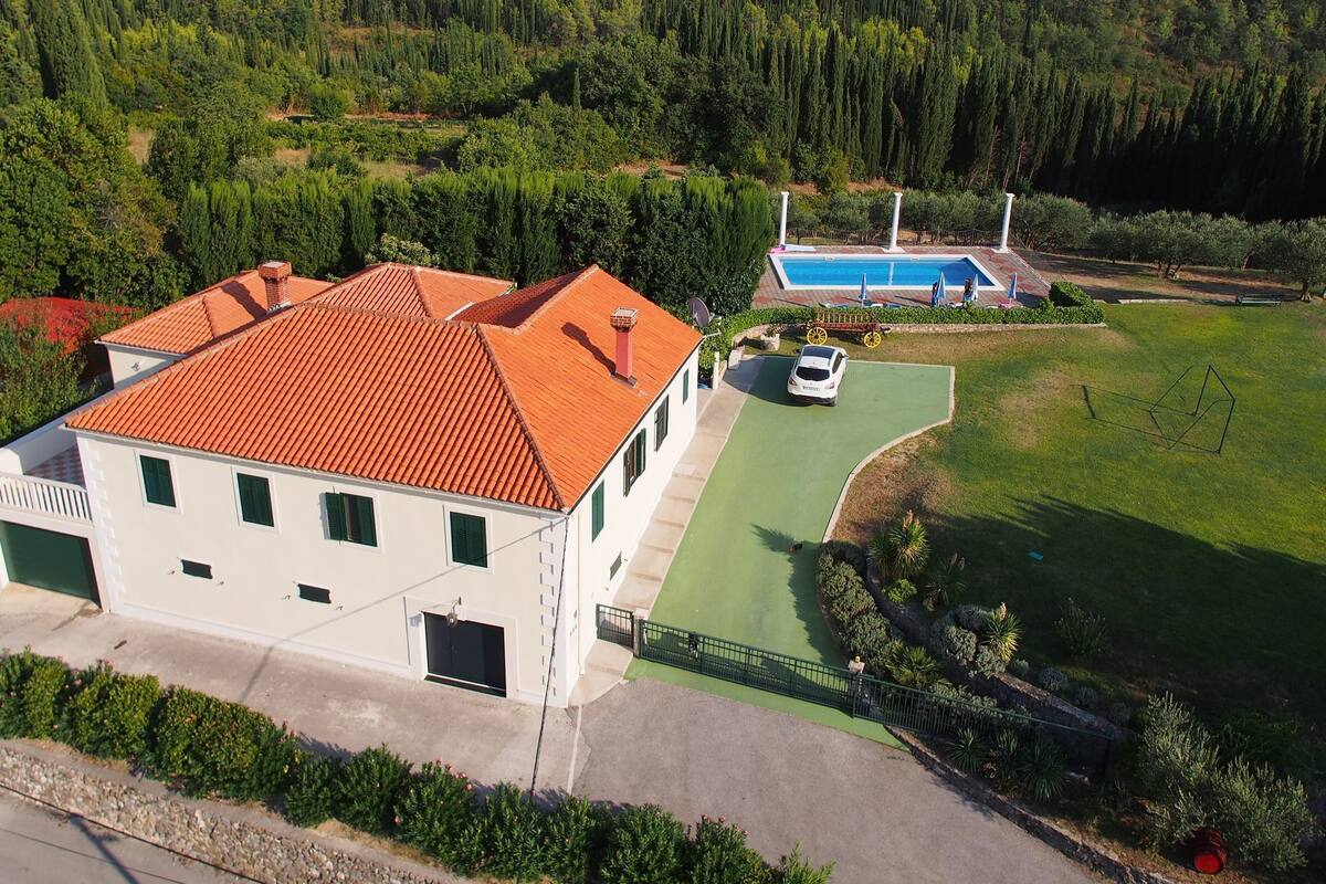 A white building with a red roof, a swimming pool, and a green lawn.