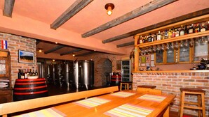 Uma área de bar com mesas de madeira, parede de tijolos e uma prateleira com garrafas e copos.