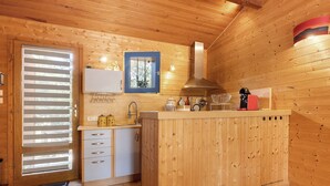 A wooden interior with a kitchen area, including a sink, cabinets, and a window with blinds. - Holiday Home "Petite Semi-Detached Villa in the Pine Forest" with Wi-Fi (Lacanau)