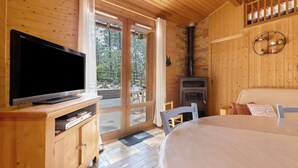 A wooden cabin with a TV, a fireplace, a bed, and a view of the outdoors. - Holiday Home "Petite Semi-Detached Villa in the Pine Forest" with Wi-Fi (Lacanau)
