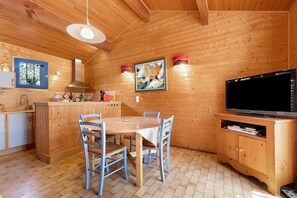Un interior de madera con una mesa de comedor, sillas, un televisor y una zona de cocina.