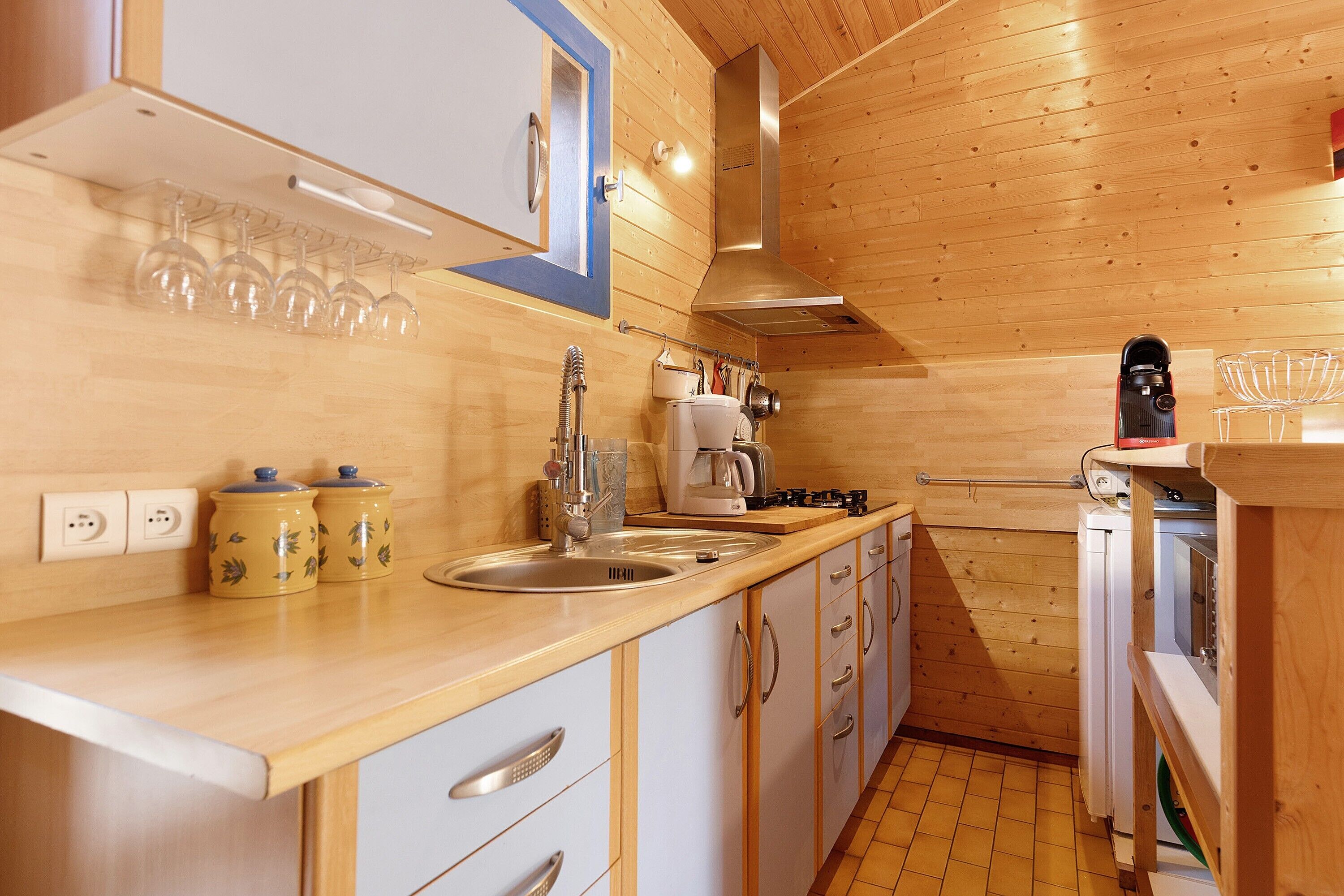 A compact kitchen with wooden walls, a sink, a stove, and a coffee maker.