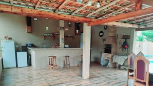 A kitchen with a tiled floor, wooden stools, a refrigerator, a small oven, and a brick oven.
