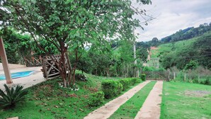A pathway leading through a lush garden with a pool and a wooden structure.