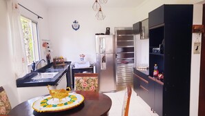 A kitchen with a dining table, chairs, a refrigerator, and a TV stand.