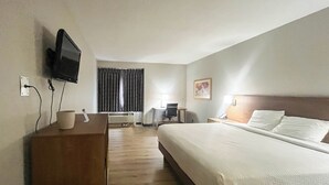 Una habitación de hotel con cama, escritorio, silla, televisor y ventana con cortinas.