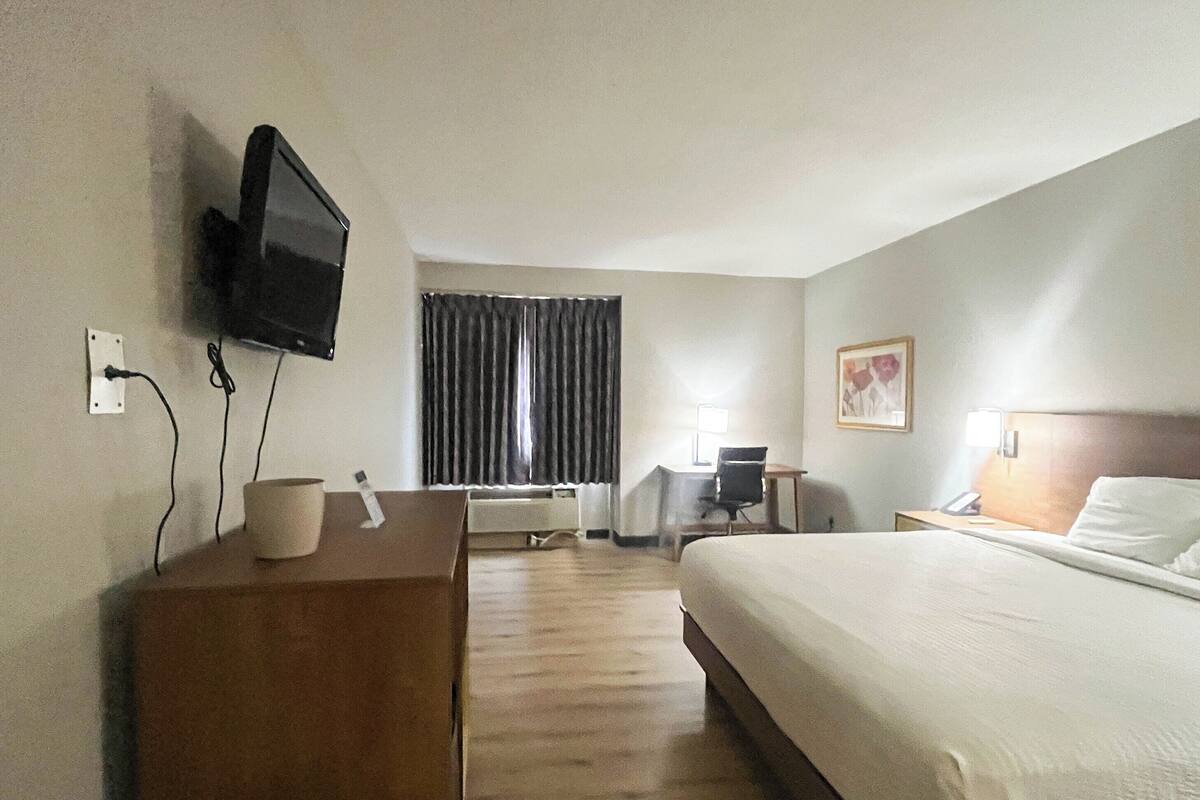 A hotel room with a bed, desk, chair, television, and a window with curtains.