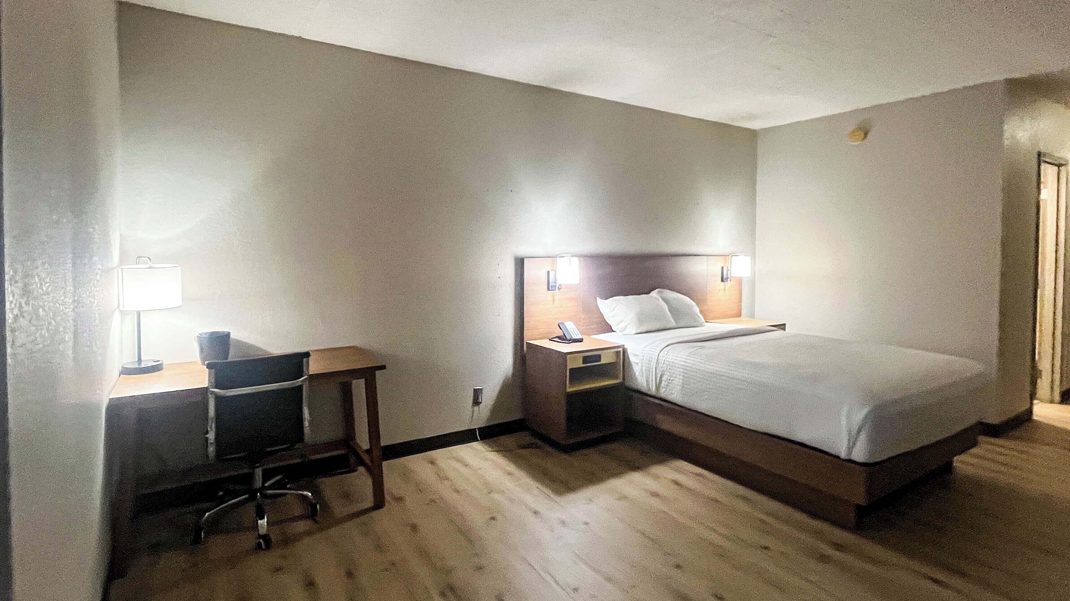 A hotel room with a bed, bedside table, lamp, desk, and chair.