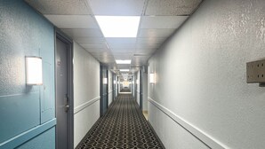 Un pasillo largo y estrecho con alfombra estampada, paredes de colores claros e iluminación empotrada en el techo.