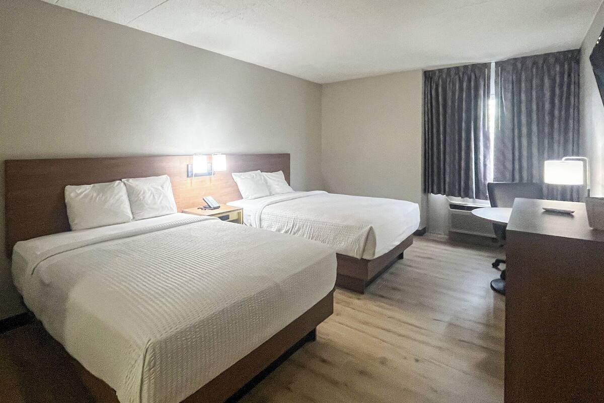 A hotel room with two beds, a desk, a chair, a lamp, and a window with curtains.