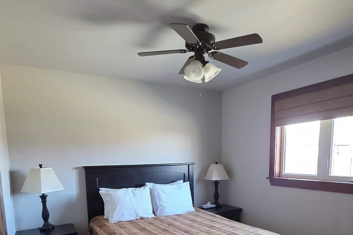 A bedroom with a bed, two bedside tables with lamps, a ceiling fan, and a window.