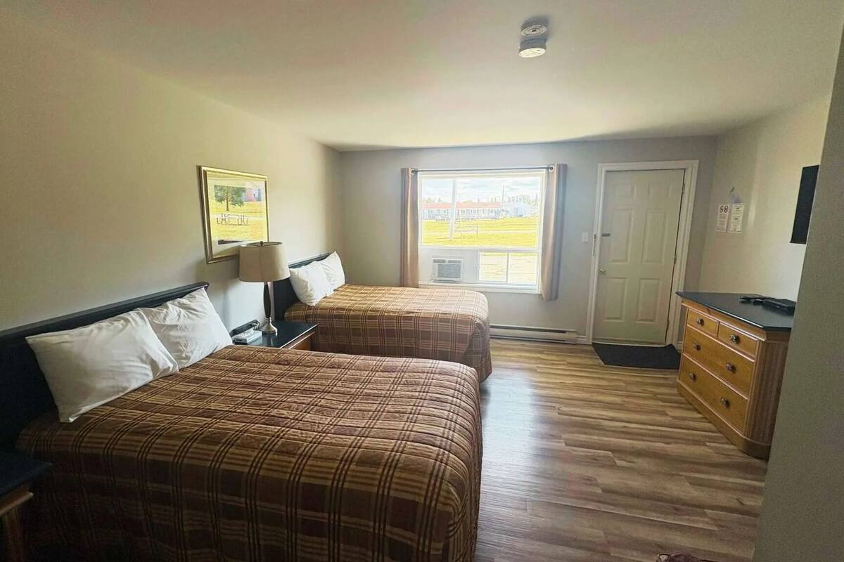 A hotel room with two beds, a dresser, a window with a view, and a ceiling light.
