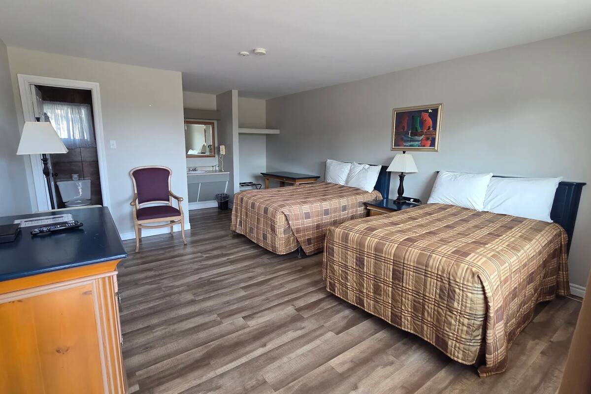 A hotel room with two beds, a desk, a chair, a painting, and a bathroom visible through an open door.