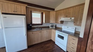 A kitchen with wooden cabinets, a refrigerator, a stove, and a microwave. - Motel & Chalets l'Acadien sur mer (Petit-Rocher)