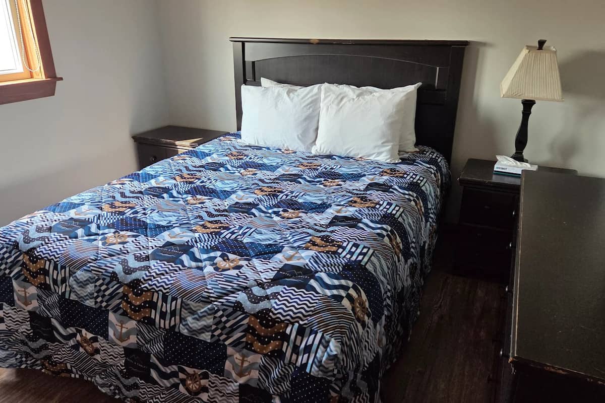 A bed with a patterned bedspread, a nightstand with a lamp, and a dresser.