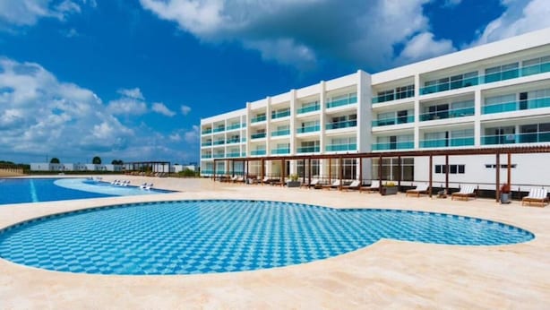 A hotel with a large pool area, multiple balconies, and a clear sky.