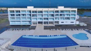 A modern hotel with multiple floors, a central courtyard with a swimming pool, and a view of the ocean.