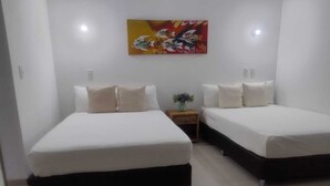 A hotel room with two beds, a small bedside table with a vase, and a colorful painting on the wall.