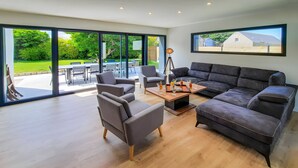A spacious living area with a large sofa, two armchairs, a coffee table, and a dining table.