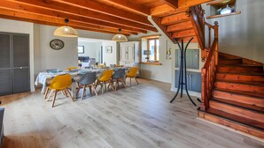 A spacious dining area with a wooden staircase and a view of the kitchen.